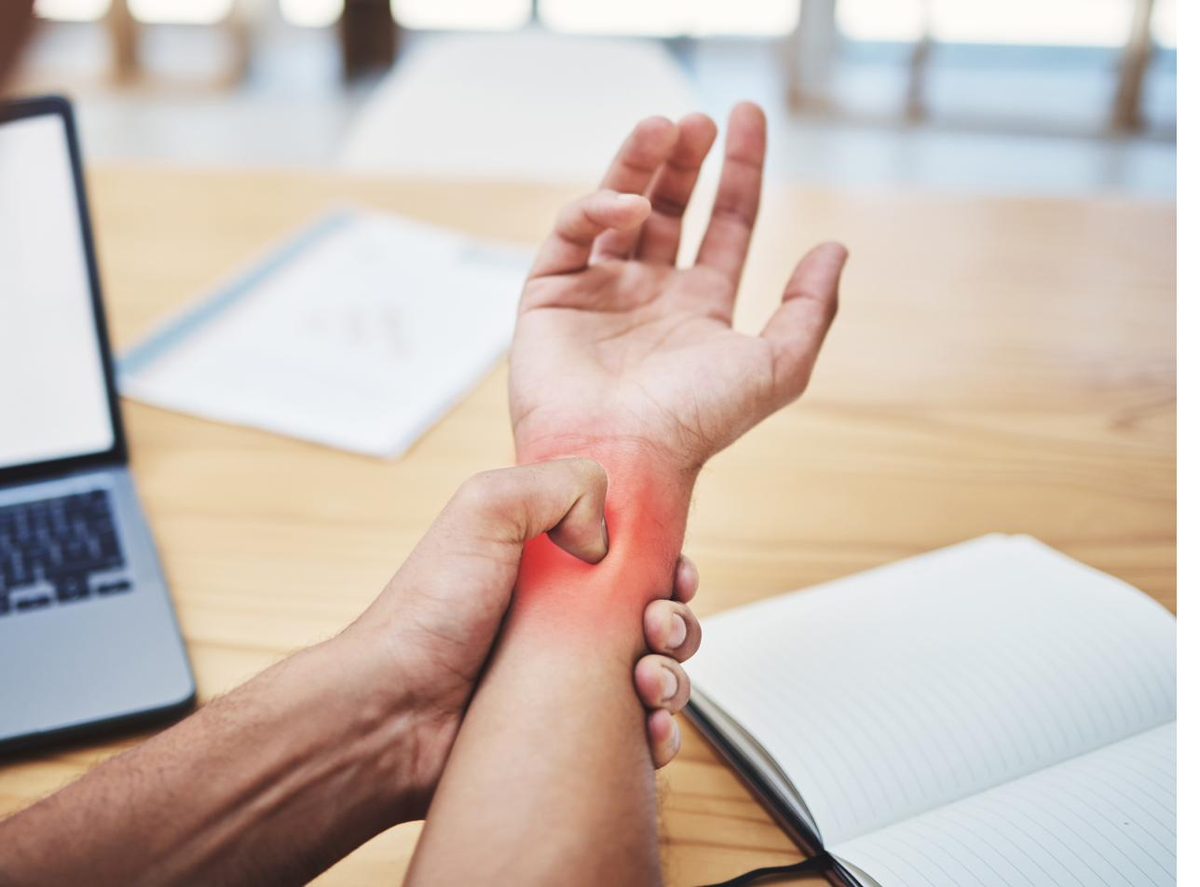 Man with wrist pain at a laptop holding his aching wrist — acupuncture for carpal tunnel syndrome in Boca Raton by Ronen Rosenblatt Nir